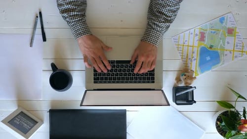 Male Arms Typing Text on Laptop Keyboard at White Wooden Desk