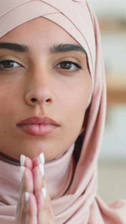 Ernsthafte konzentrierte indische Muslimin mit rosafarbenem Hijab betet und schaut zu Hause in die Kamera