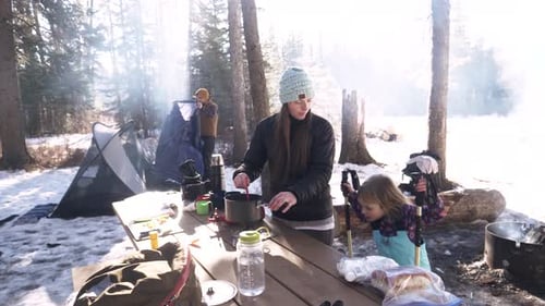 Woman cooking on camping stove in snowy forest of Canada slow motion