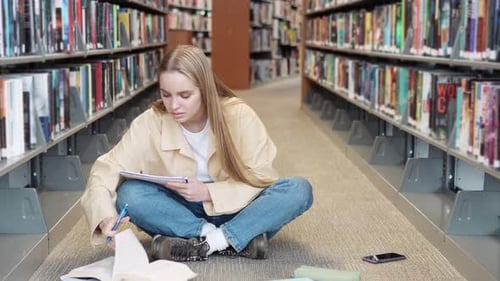 Girl Student Sitting on Floor in University Library Learning Writing Notes
