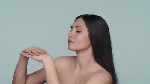 A Woman Enjoys the Velvety and Softness of the Skin of Her Hands in the Studio on a Blue Background