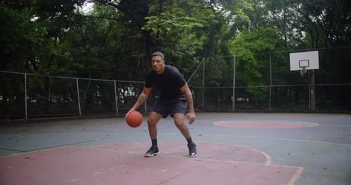 Homme hispanique dribble au basket sur un terrain extérieur, faisant preuve de concentration, de mouvement et de détermination pendant