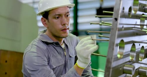 Un technicien asiatique de sexe masculin inspecte les fixations métalliques de près, vérifiant le placement de la tige de guidage,