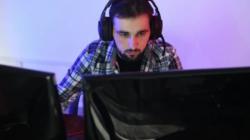 Spieler mit Kopfhörern sitzt vor buntem Hintergrund und schaut auf Monitore