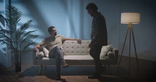Two Men Talking on Couch Indoors at Night
