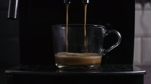 A close-up view of a glass cup being filled with freshly brewed espresso from a coffee The rich
