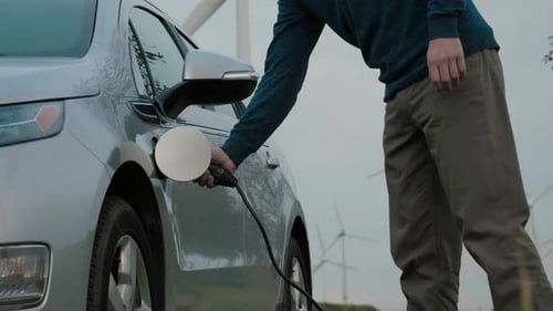 Man Unplugs Electric Car near Wind Turbines