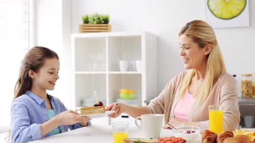 Mother gives slice of cake to daughter in kitchen