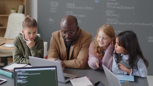 Teacher Helps Young Students with Coding on Laptop