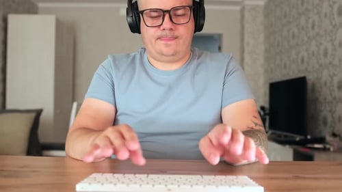 Man Typing on Keyboard Wearing Headphones Indoors