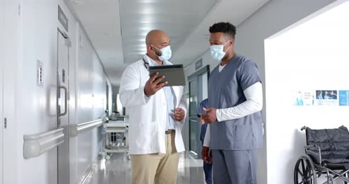 Diverse doctors discussing work and using tablet in corridor at hospital, slow motion