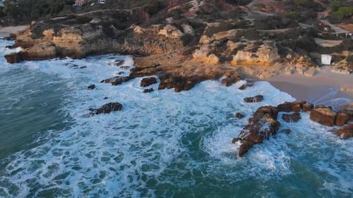 Aerial drone pan view of low tide waves hitting the shoreline, located in coastal city Albufeira, Po
