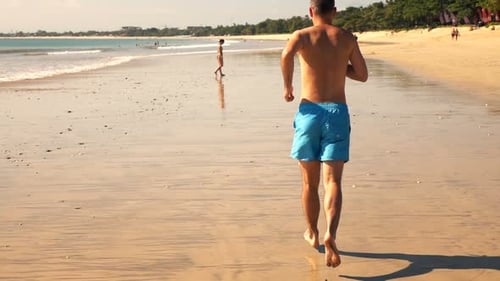 Young man runs on sandy beach in super slow motion on a sunny summer day