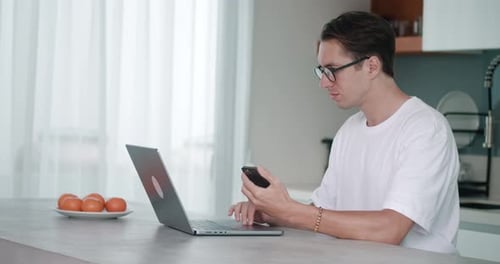 Young Adult Using Phone and Laptop at Kitchen Counter