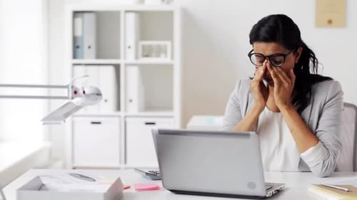 Tired Woman Rubbing Eyes at Desk with Laptop
