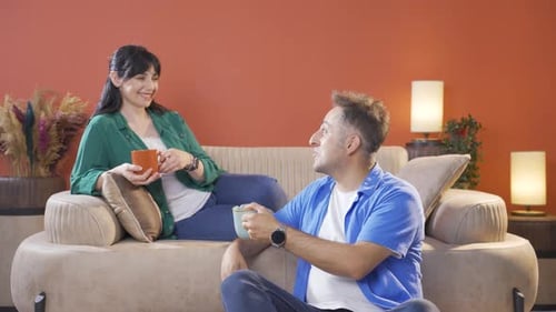 Couple Conversing and Drinking from Mugs at Home