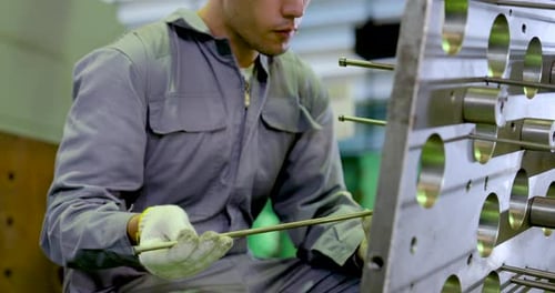 Un technicien asiatique mesure une tige de guidage métallique à côté de la plaque de fixation, examine l'alignement et l'usinage