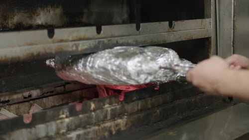 Slow motion of cook putting foil wrapped meat into charcoal grill.