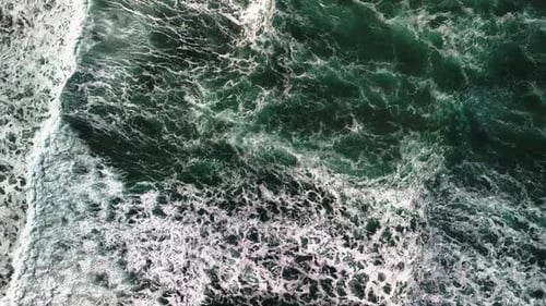 High aerial, slow motion view of powerful waves with white caps crashing on beautiful, scenic beach