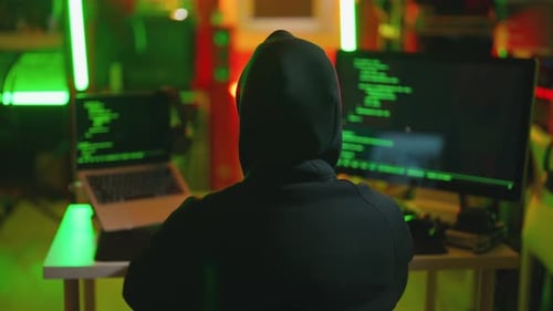 Hooded Figure Coding at Computer in Dark Room