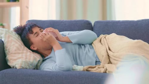 Femme malade de la grippe sur un canapé à la maison, éternuant et se mouchant