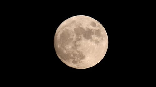 Leuchtend orangefarbener und gelber Vollmond vor einem dunkelschwarzen Himmel, der sich diagonal von der Bildmitte bewegt