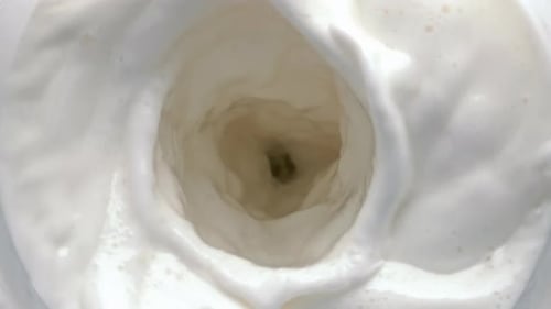 Wirbelnde, bewegliche Ansicht von oben auf das Laktosegetränk. Saubere Milch rotiert hinein