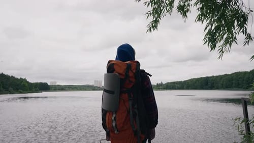the traveler stands on the background of the river and the city with sports equipment rear view
