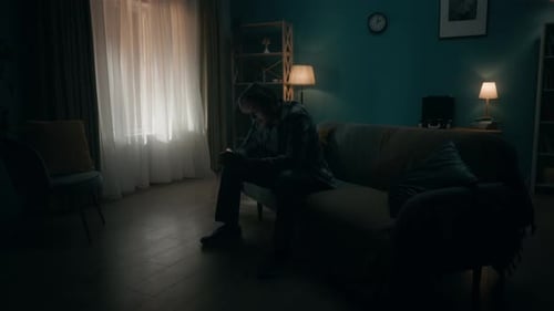Smartphone Addiction and Depression A Young Man Sits in a Dark Room on a Sofa with a Phone in His