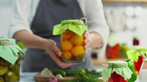 Holding Jar of Preserved Yellow Tomatoes in Kitchen