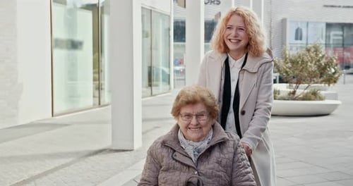 Woman Pushing Senior in Wheelchair in Urban Setting