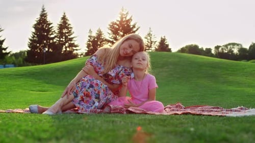 Positive Family Enjoying Sunset Time in City Park. Young Mother Hugging Daughter