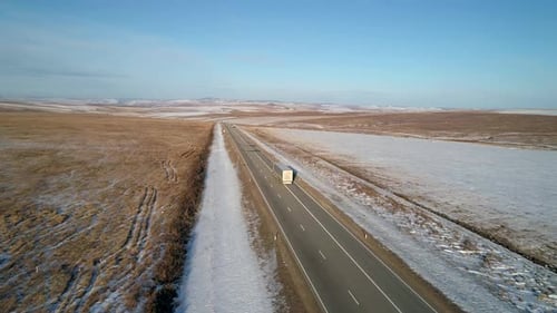 Luftaufnahme einer Intercity-Straße mit fahrendem LKW, umgeben von schneebedeckten Feldern im Winter
