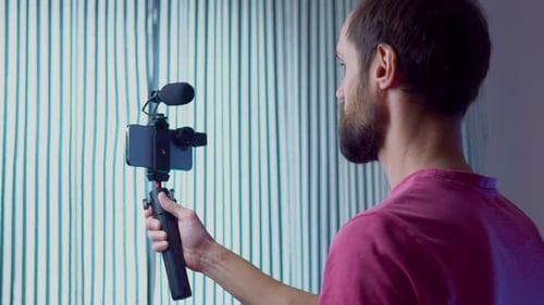 A Young Blogger Records a Video with Himself on His Smartphone in His Room Studio