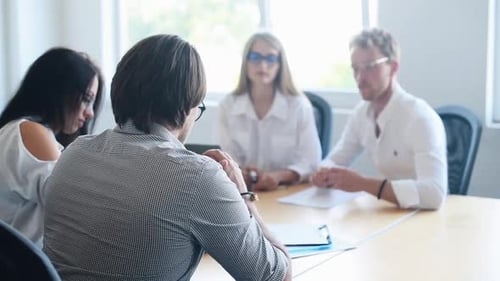 Young business people in formal clothes sitting by the table and working in the office with document