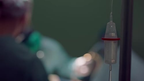 Closeup Medical Dropper with Blurred Surgeon and Nurse Performing Operation at Background