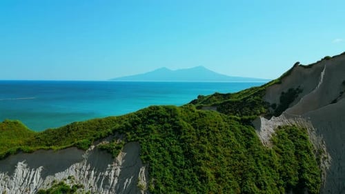 Green slopes meeting blue ocean aerial view. Clip. White cliffs and blue shore