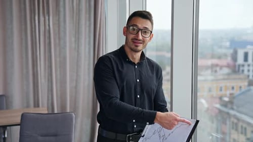 Businessman in black shirt, trousers and glasses holding a paper with chart.