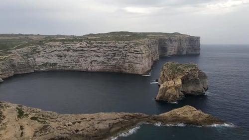 Stunning aerial shot of rocky cliff in Malta. Drone fly along coastline in a cloudy day.