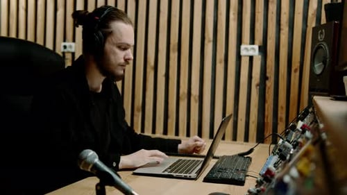 young sound engineer with headphones working in a music studio with monitors and an equalizer