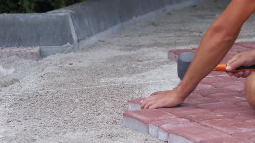 Man lays red brick pavers on gravel