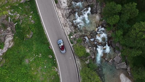 Car Travels Along Scenic Mountain Road by a Stream