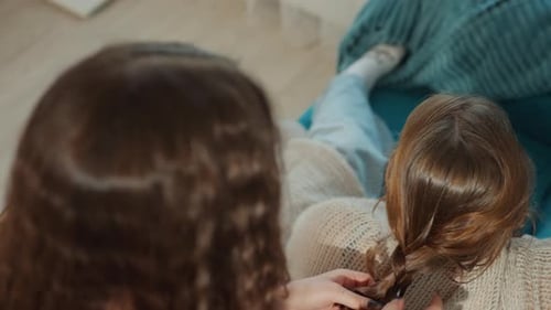 White Mother Braiding Hair On Couch Knitted Sweater Warm Livingroom Light Closeup Hands Weaving
