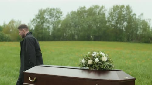 Man Walking Near Coffin in Grassy Field