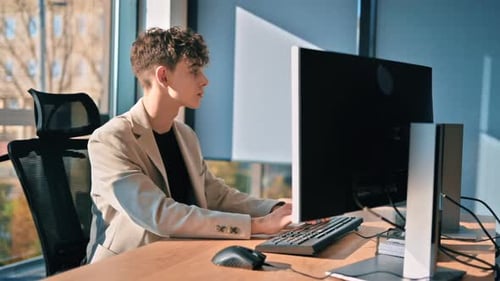 Young man is working in a computer in an office, windows on the background