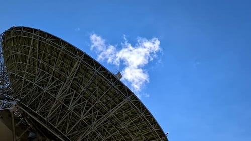 Large radio telescope pointed at clear blue sky with a single cloud passing above