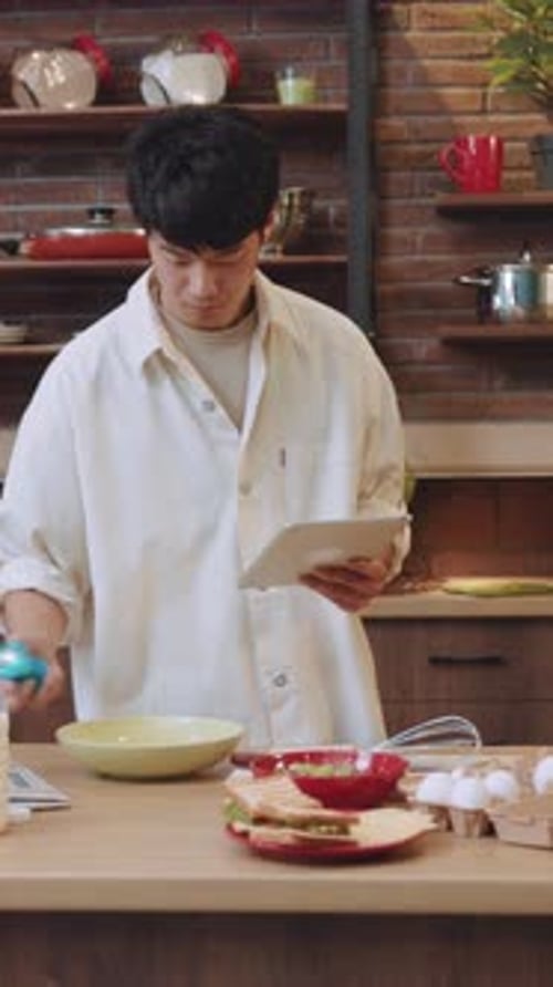 Young Adult Follows Cooking Recipe in Kitchen