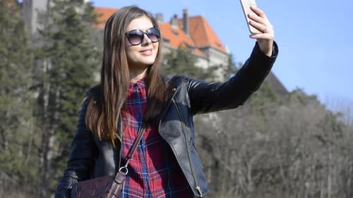 Pretty young brunette girl with sunglasses taking selfies with a castle in a public park.