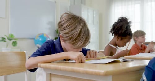 Zeitlupenaufnahme junger Grundschüler, die in Notizbuch mit Bleistift am Holztisch schreiben, diverse