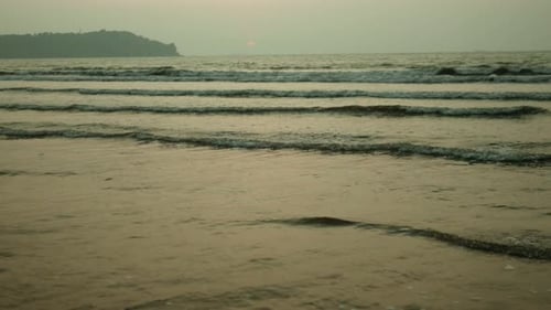 Sunset view over the calm sea with gentle waves and distant headland, serene evening ambiance